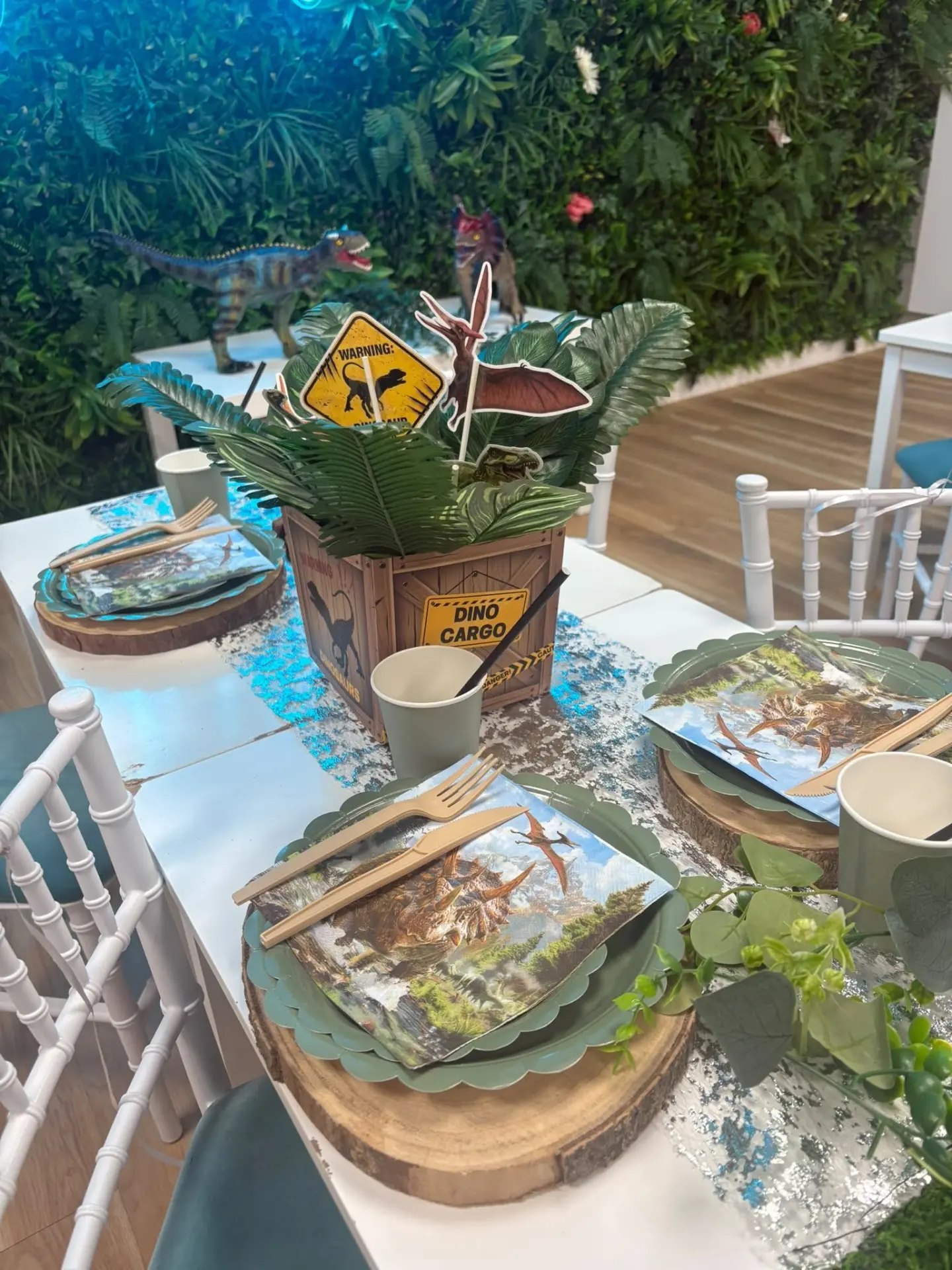 A dinosaur party table setting with wood slice place mats, dinosaur napkins and a fern centrepiece