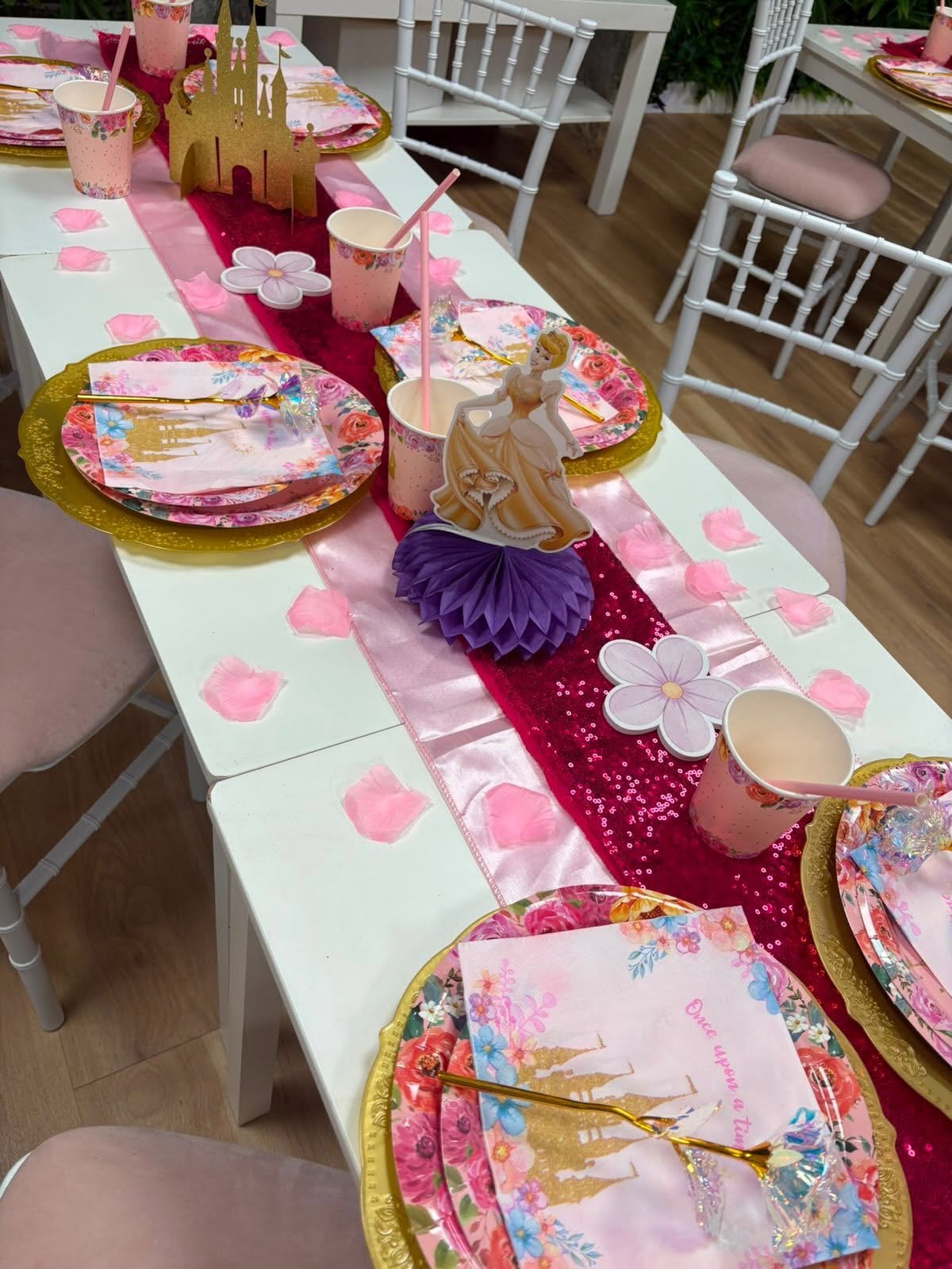 A princess party table setting with pink and magenta runners, rose petals and a gold castle centrepiece
